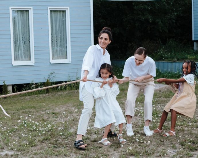 A happy family enjoys a game of tug of war in a grassy field by a house.