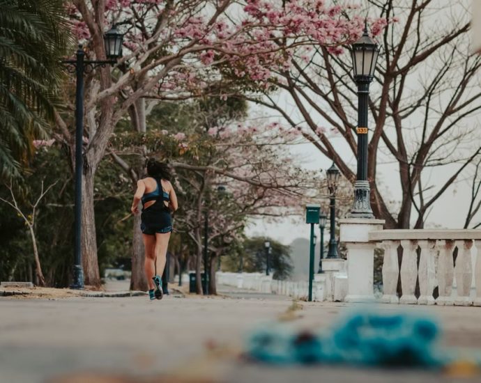 A woman jogs through a picturesque park lined with blooming spring trees and vintage lamps.