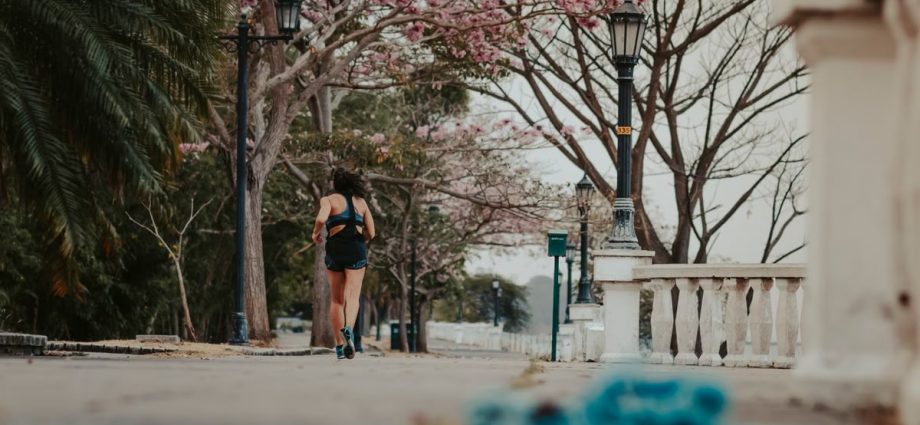 A woman jogs through a picturesque park lined with blooming spring trees and vintage lamps.